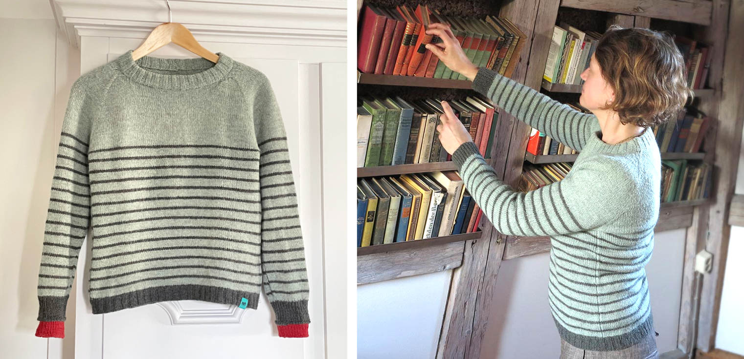 Julia trägt den grünen gestreiften Wollpullover mit dem Namen Nürnberg vor einem Bücherregal stehend. Sie greift nach einem Buch.