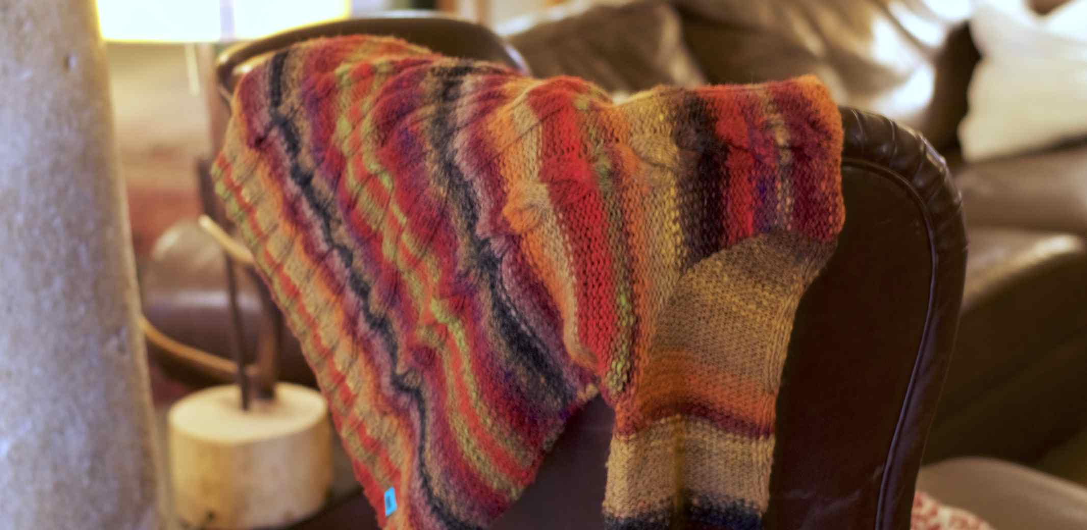 Wollpullover Tokyo aus japanischer Wolle in Herbstfarben auf einem Ledersofa
